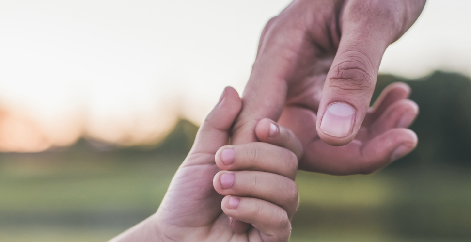 Small child's hand holding index finger of adult's hand