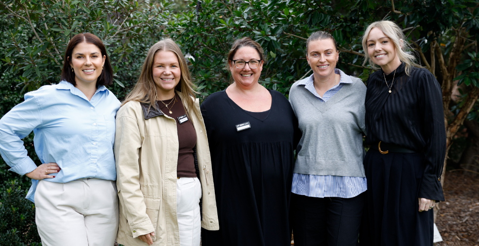 5 females standing side by side smiling at camera
