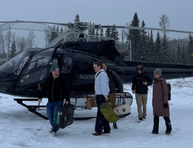 Five people exiting a black helicopter on snow