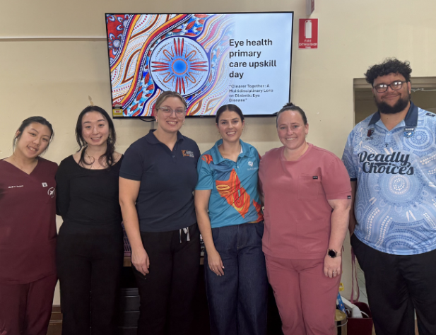 Six people standing side-by-side in front of a TV screen with Indigenous artwork and text saying, "Eye health primary care upskill day"