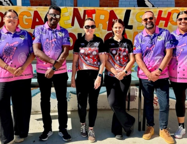 Six people smiling at the camera, standing in front of sign saying "Goodooga Central School"