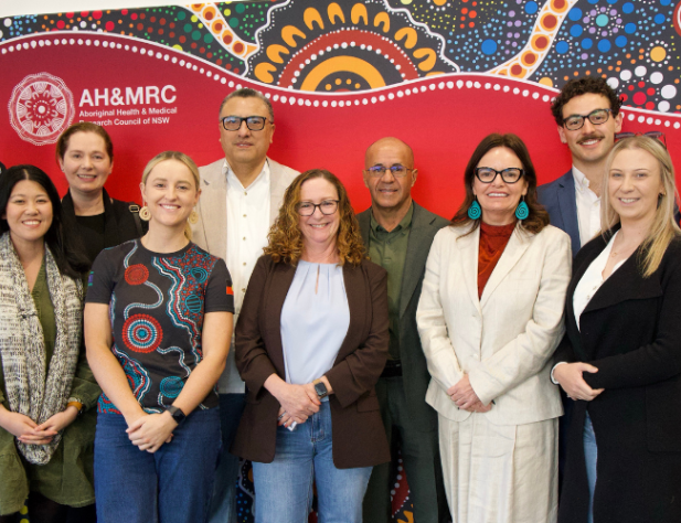 Eleven people standing in front of Indigenous art background, smiling at the camera
